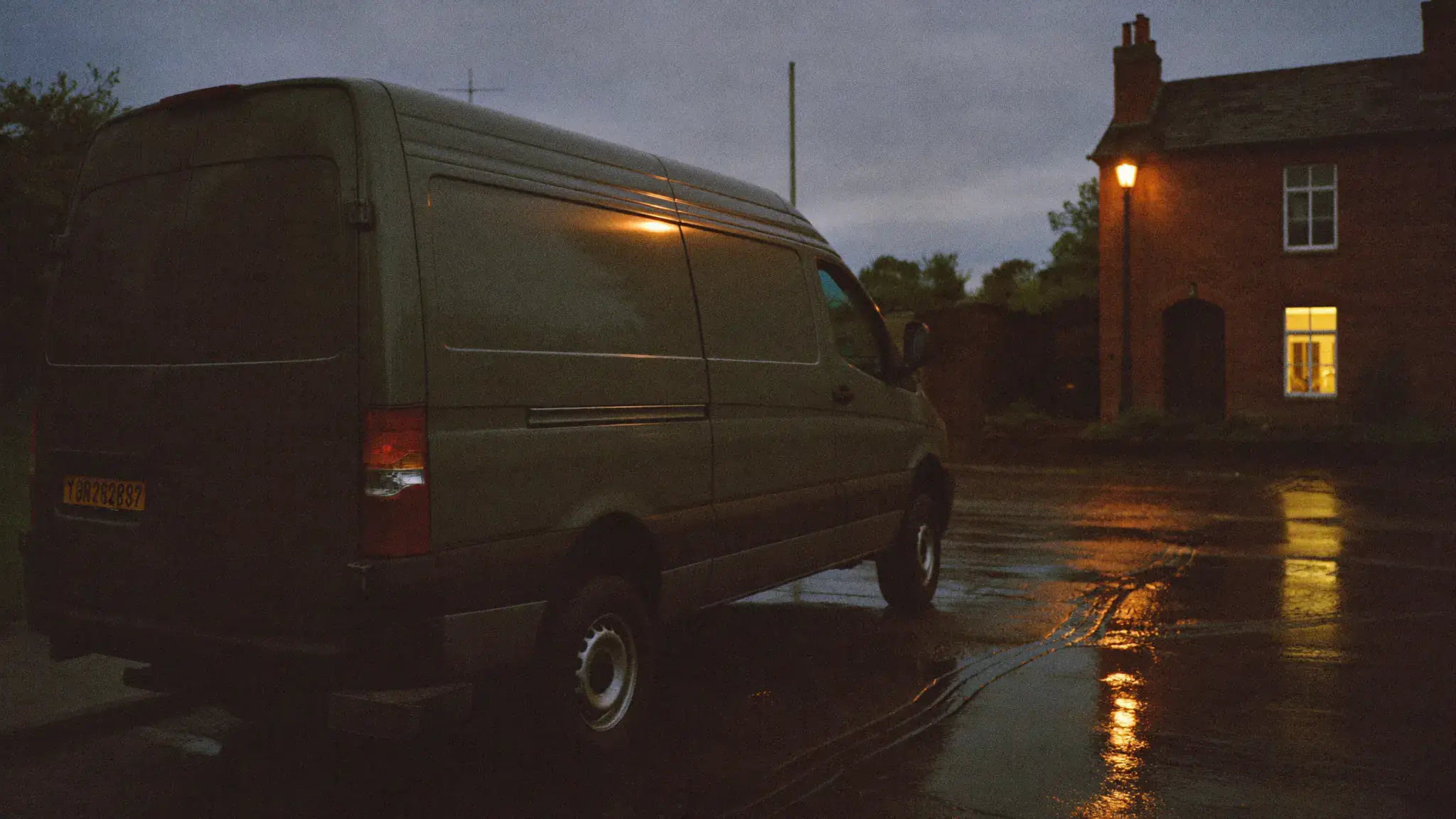A tradesman's van parked on a Dublin street at blue hour with one warm lit window behind it